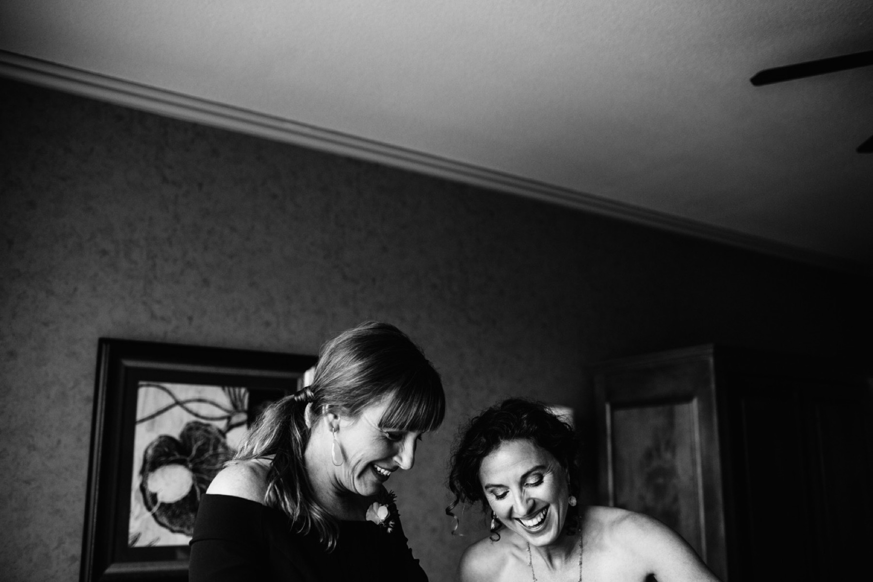 bride and bridesmaid laugh as she's getting into dress