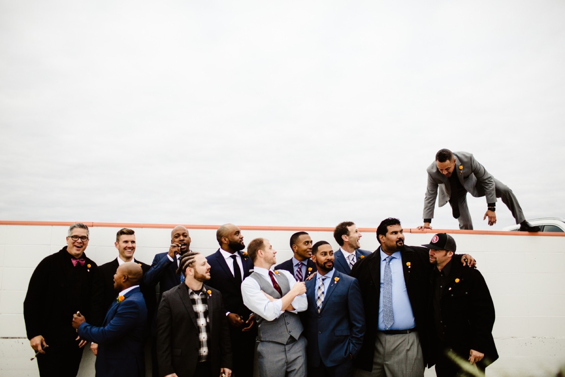 groomsmen with one groomsman jumping over wall