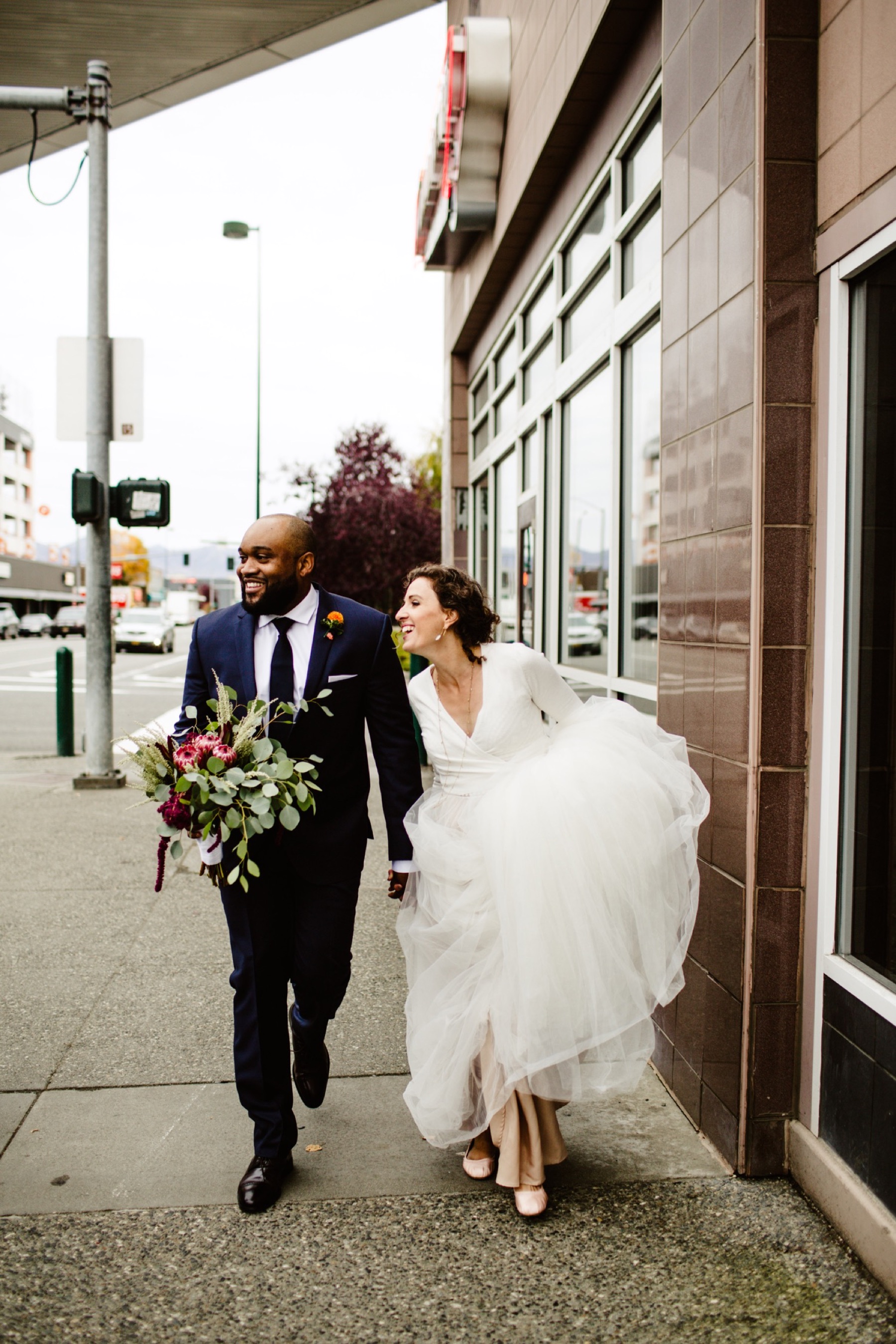 bride and groom walk down sidewalk in downtown anchorage