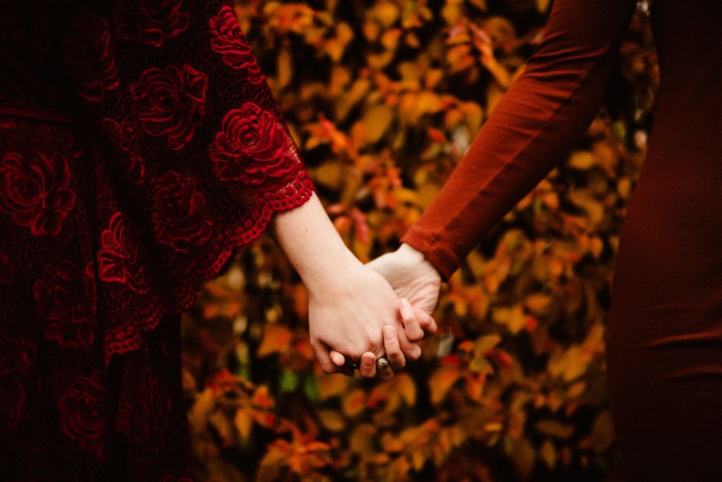 sisters hold hands with vibrant fall leaves behind 