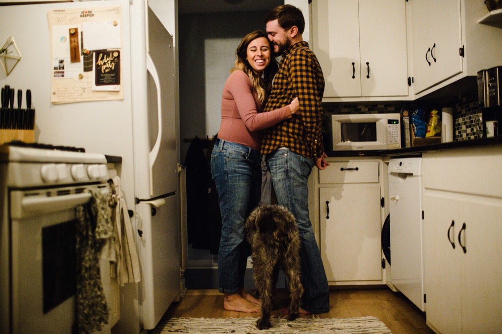 couples embraces in kitchen with dog in the foreground 