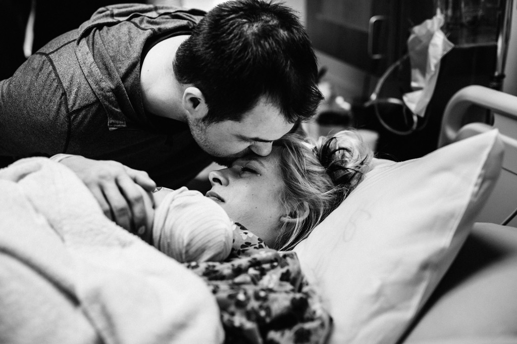 husbband kisses wife as she holds their newborn baby at alaska regional hospital