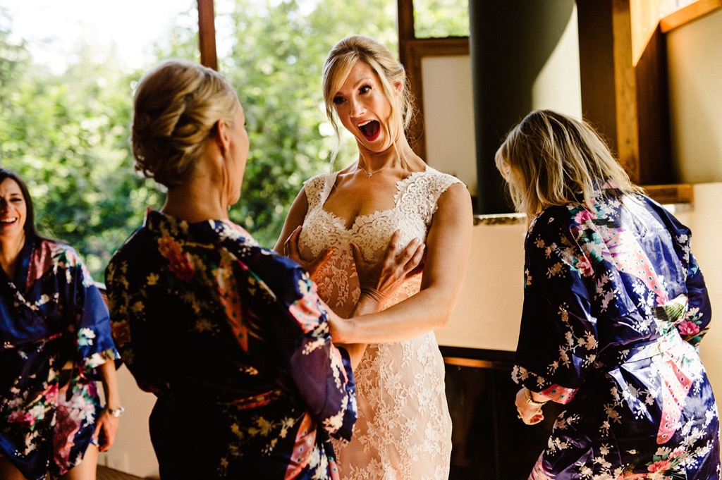 bridesmaid playfully holds brides boons while getting ready 