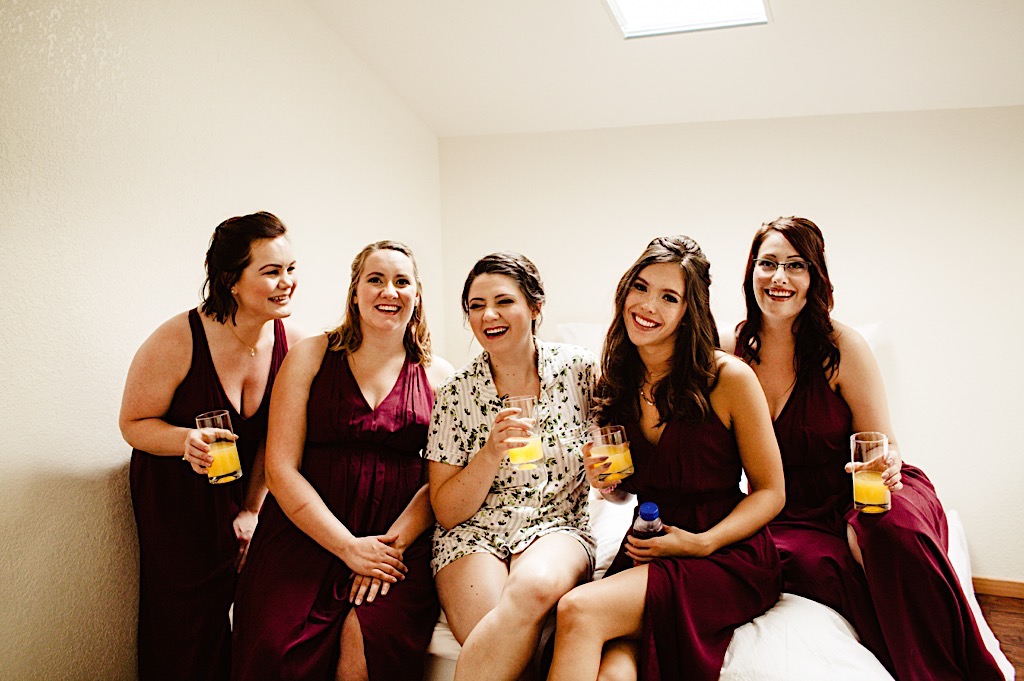 bridal party sitting on bed holding mimosas