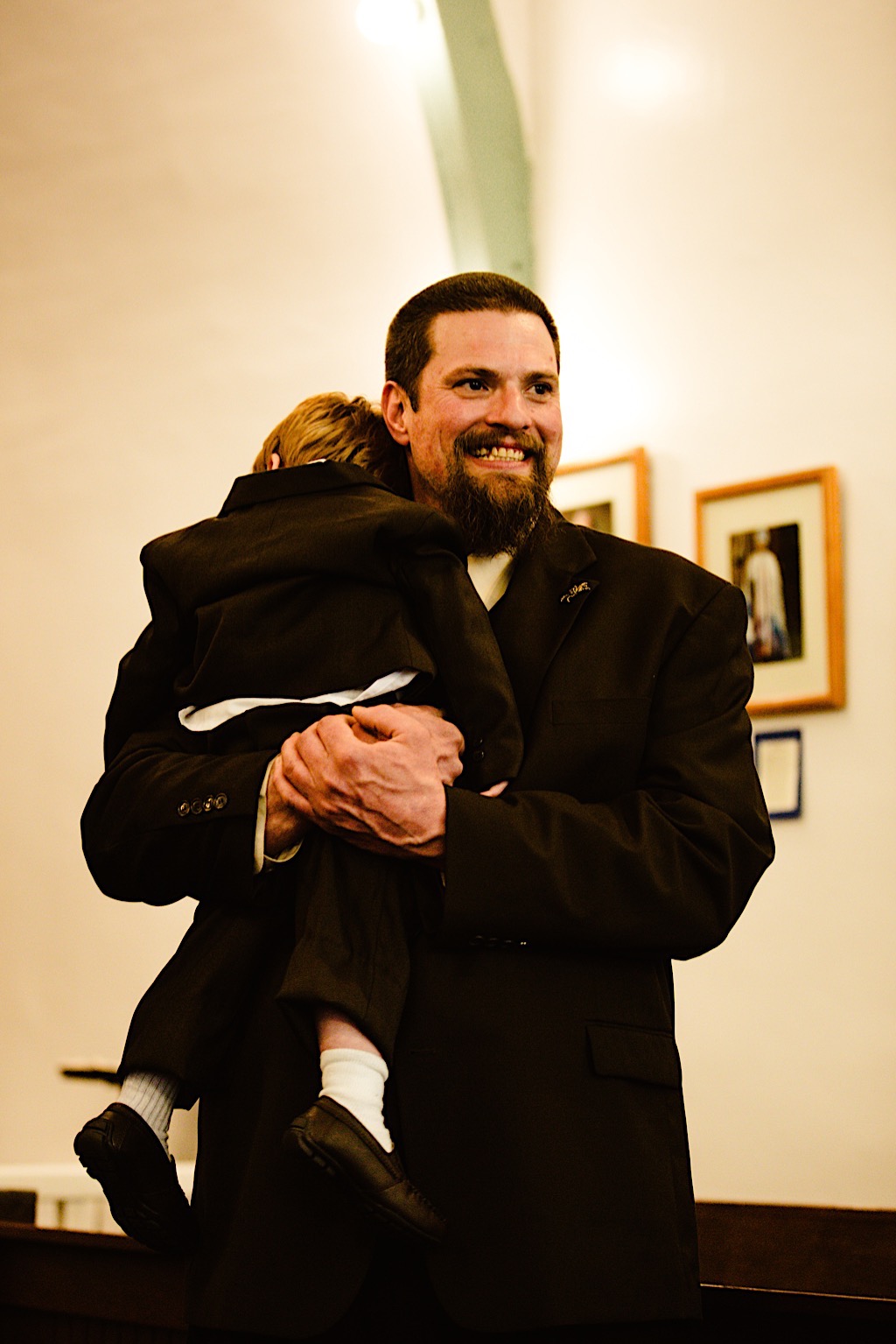 groom holding young in his arms while bride comes down aisle 
