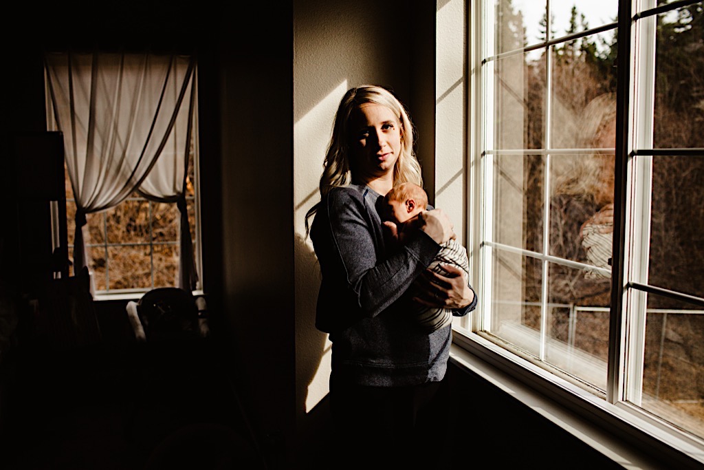 mother holding newborn baby by window 