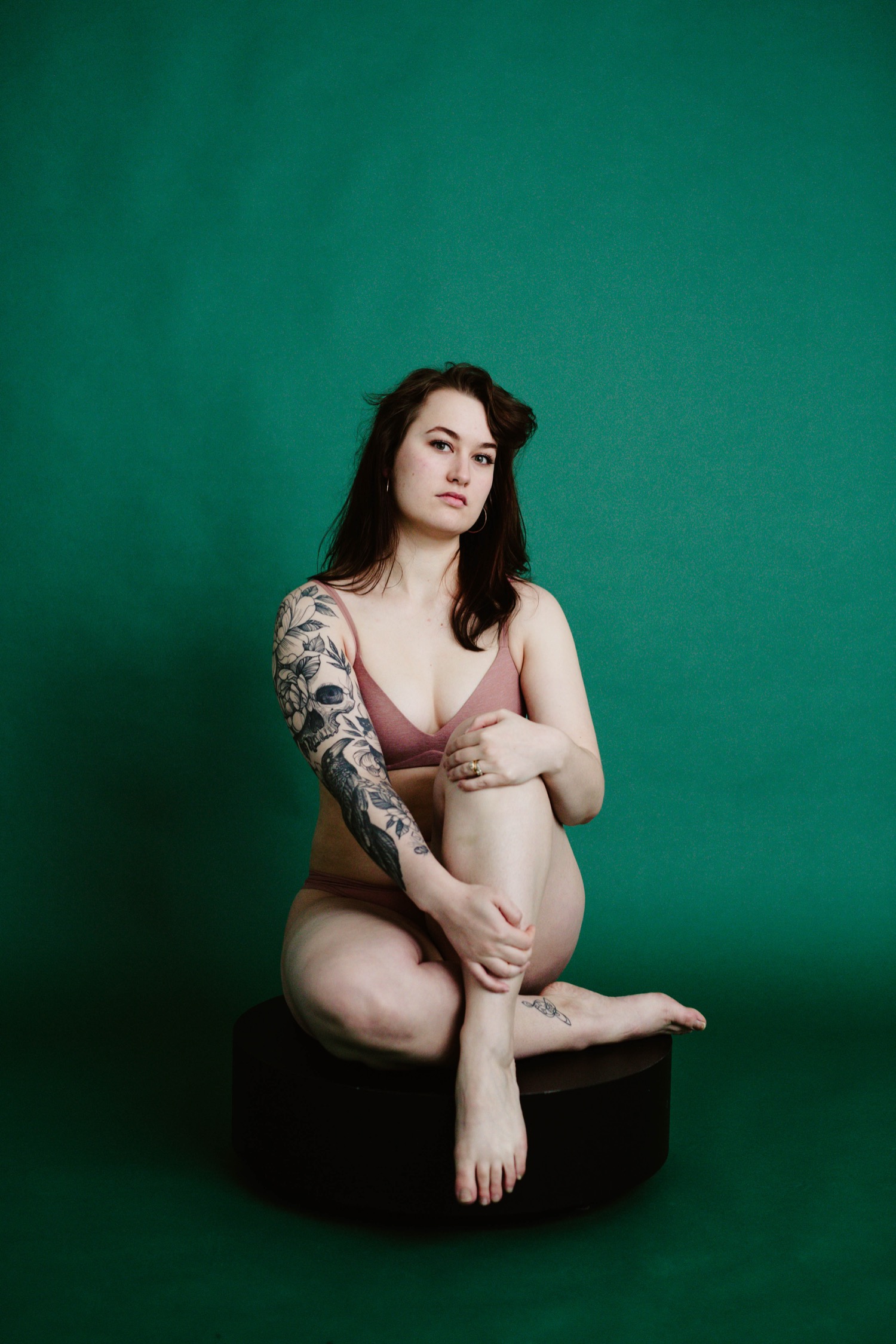 woman with tattoos sits in front of green backdrop