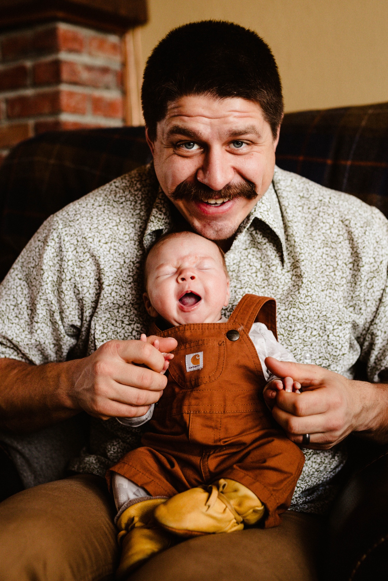 dad smiling at camera holding yawning baby